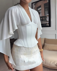 Person wearing a white outfit with ruffled sleeves in a room with a couch and framed picture.