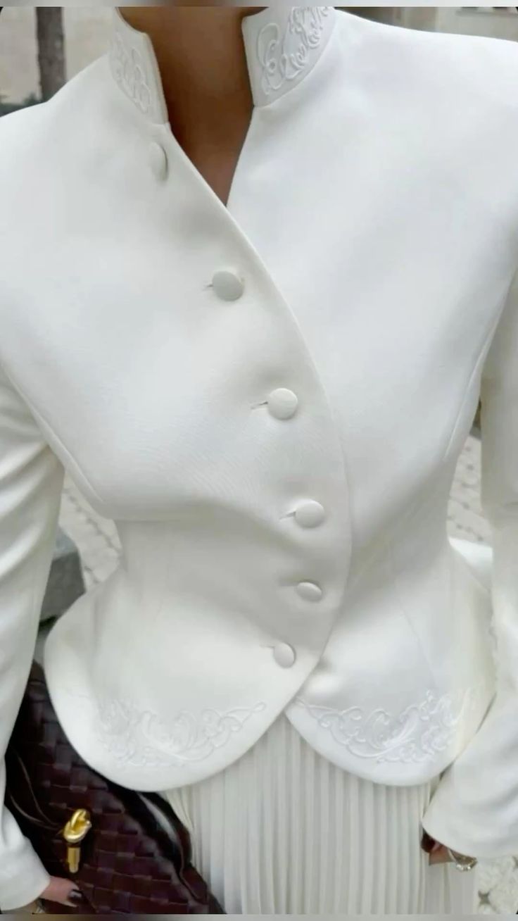 Close-up of a white blazer with decorative buttons and lace details.