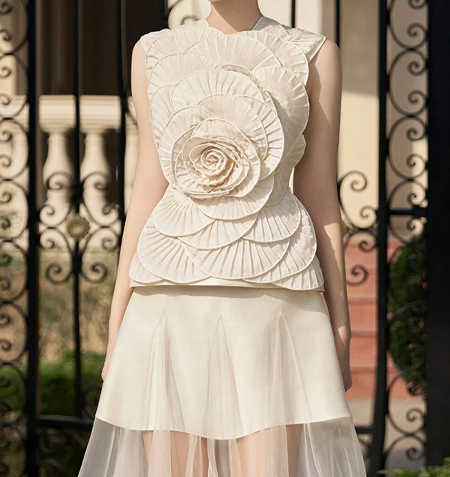 Woman wearing a white floral top and skirt in front of decorative metal gates.