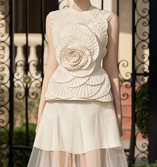 Woman wearing a white floral top and skirt in front of decorative metal gates.