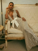 Model wearing a silver sequined V-neck gown with a white bow.