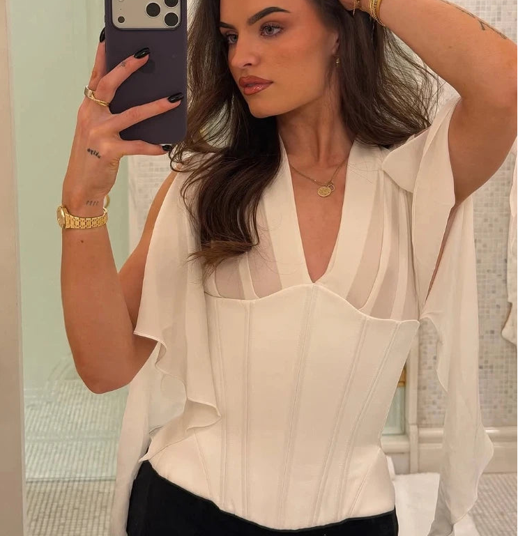 Woman taking a mirror selfie wearing a white blouse with sheer panels.