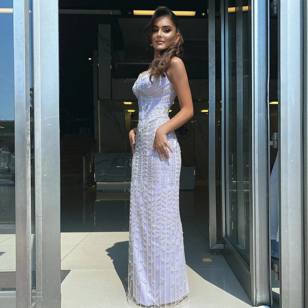 Woman in a white evening gown standing in front of a modern building entrance.