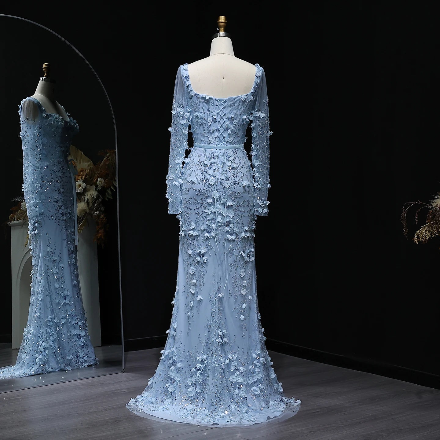 Light blue evening gown with floral embellishments on a mannequin against a dark background.