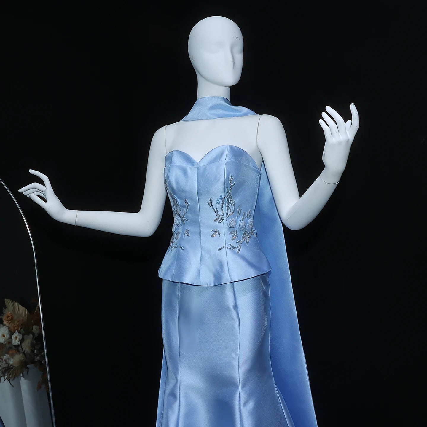 Mannequin wearing a light blue evening gown with floral embroidery on a black background