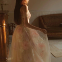 Woman in a floral dress standing in a softly lit room.