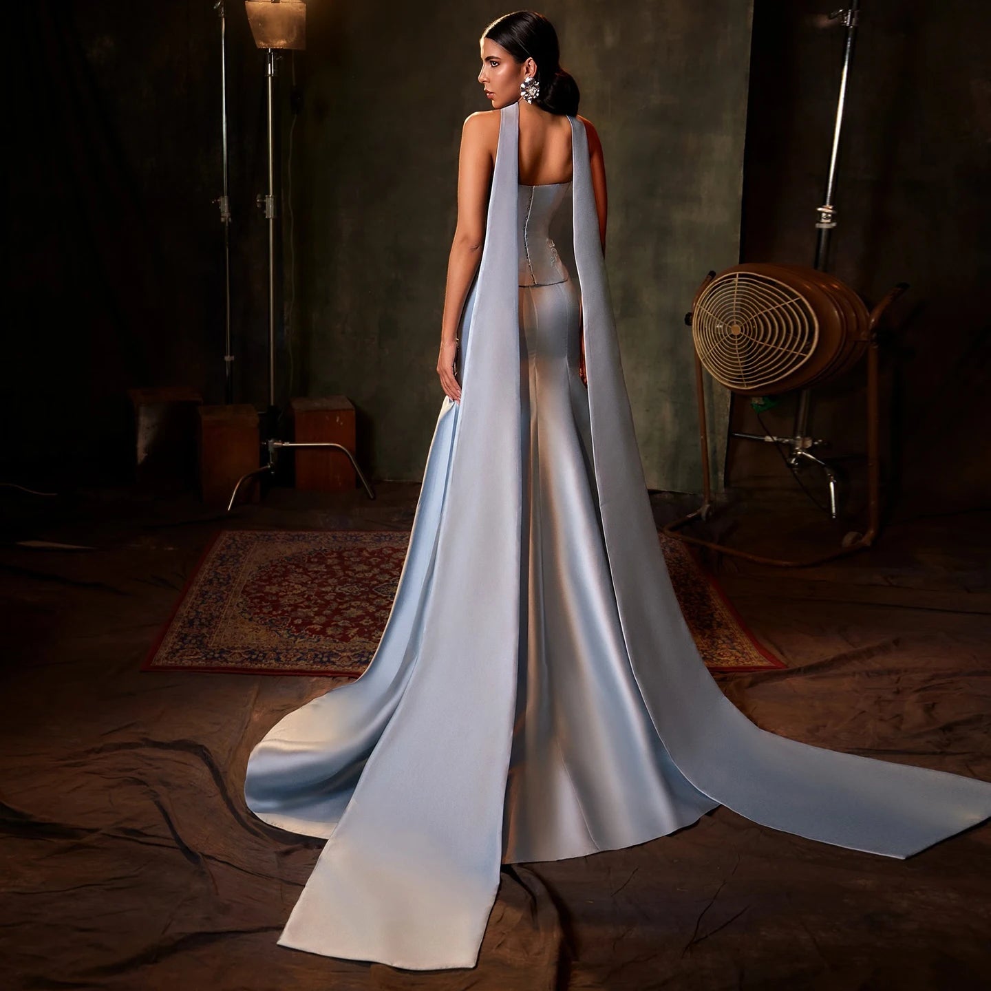 Woman in a long, flowing dress with a cape in a dimly lit room.