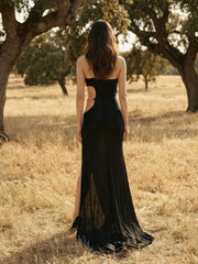 Woman in a black dress standing in a field with trees in the background
