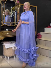 Woman in a light blue dress standing in a room with mirrors and furniture.