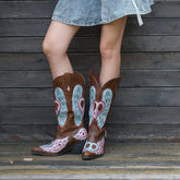 Person wearing brown cowboy boots with heart and wing designs against a wooden background