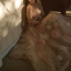 Woman in a flowing dress with floral patterns standing against a textured wall.