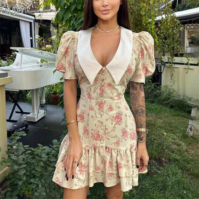 Cream mini dress with a white pointed collar, short puff sleeves, pearl button front, and a tiered ruffled hem.