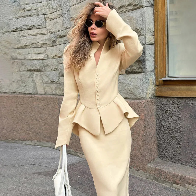 Woman in a Apricot stand collar button blazer skirt suit styled for office commute suit standing against a stone wall.