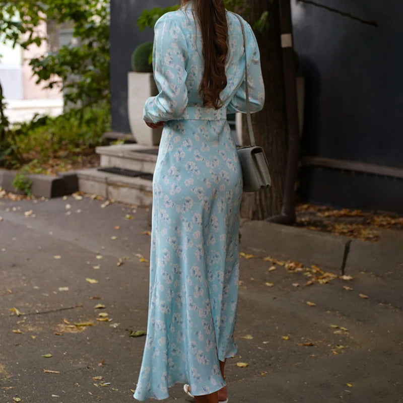 Back view of a woman summer an A-line printed dress for women – blue and floral, walking outdoors on a leafy street.