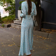 Back view of a woman summer an A-line printed dress for women – blue and floral, walking outdoors on a leafy street.