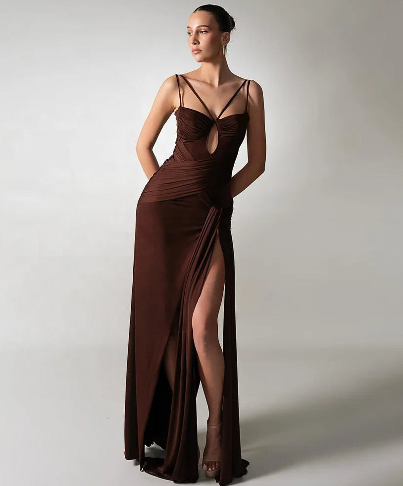 Woman wearing a long brown evening gown with a high slit on a plain background