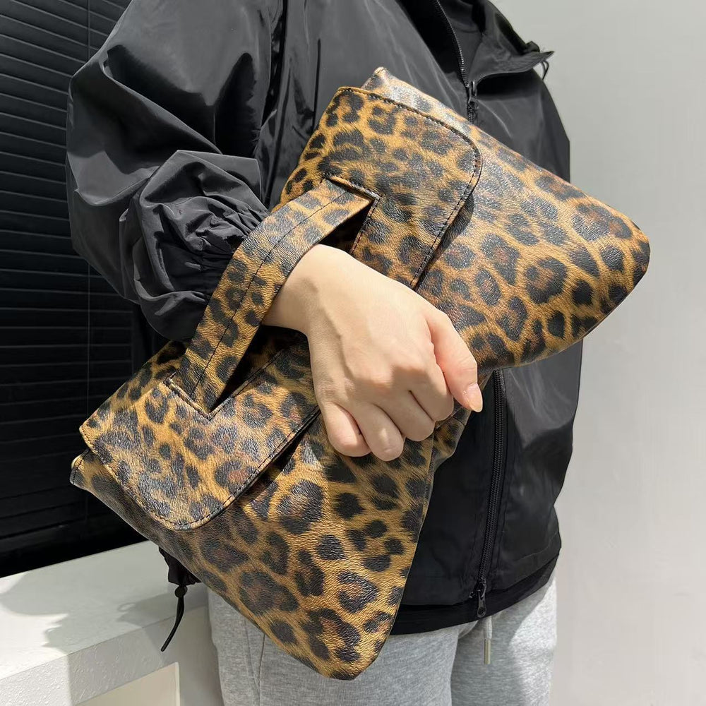 Person holding a leopard print clutch bag against a neutral background