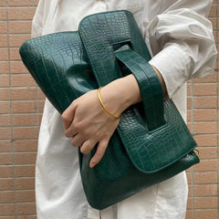 Person holding a green crocodile-patterned handbag against a brick wall.