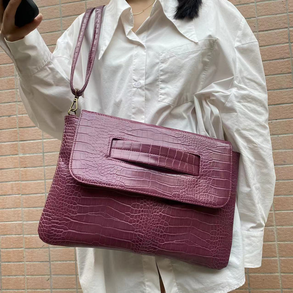 Person holding a purple crocodile-textured handbag against a brick wall.