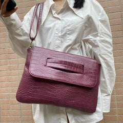 Person holding a purple crocodile-textured handbag against a brick wall.