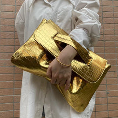 Person holding a gold clutch against a brick wall