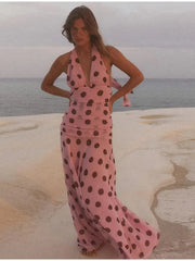 Woman in a pink polka dot dress standing on a beach.