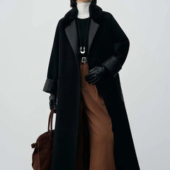 Person wearing a long black coat, brown pants, and holding a brown bag on a white background