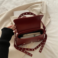 Red handbag with studded details on a white fabric background