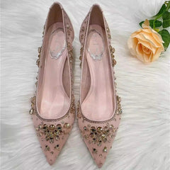 Pink high-heeled shoes with embellishments on a white surface with a yellow rose.