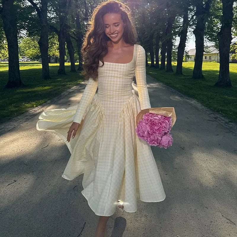 Woman in a white dress holding pink flowers on a tree-lined path