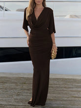 Woman in a brown evening gown standing on a dock with a white boat in the background.