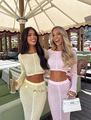 Two women in matching outfits standing under a large umbrella at an outdoor setting.
