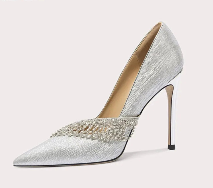 Silver high-heeled shoe with embellishments on a light gray background