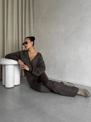 Person in a dark outfit sitting on the floor against a plain wall with a white stool.