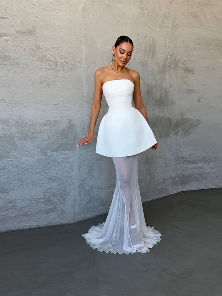 Woman wearing a strapless white dress with a fitted bodice and flowing skirt against a plain background.