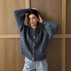 Woman wearing a gray cable knit cardigan against a wooden paneled wall