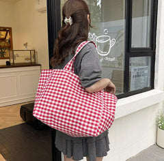 Person holding a red and white checkered bag in front of a store entrance.