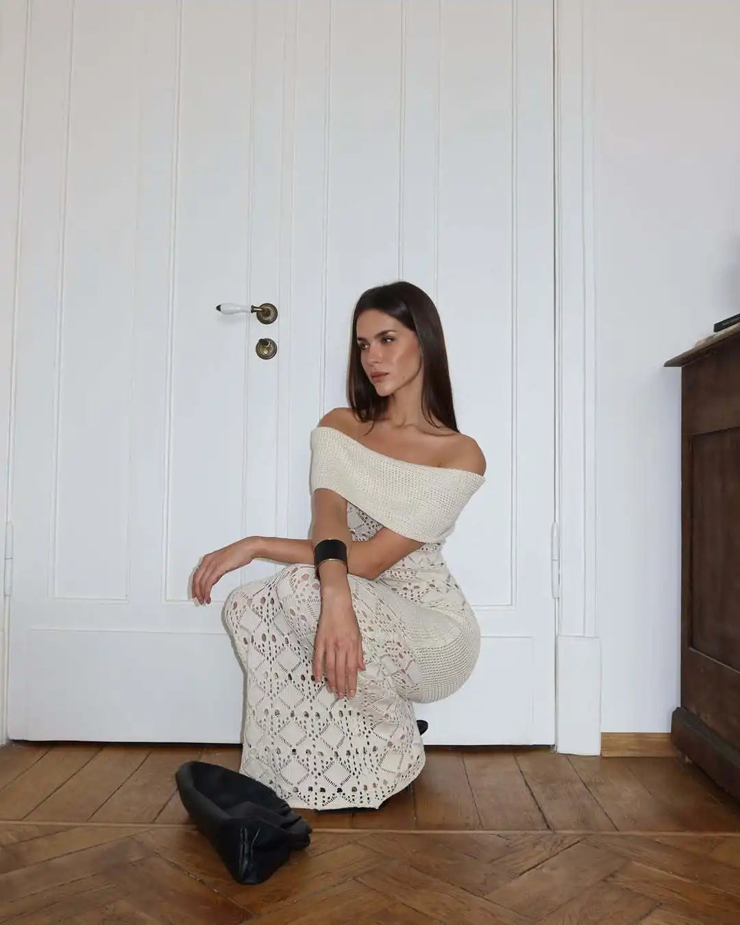 Woman in a white off-shoulder dress sitting on the floor against a white paneled wall.