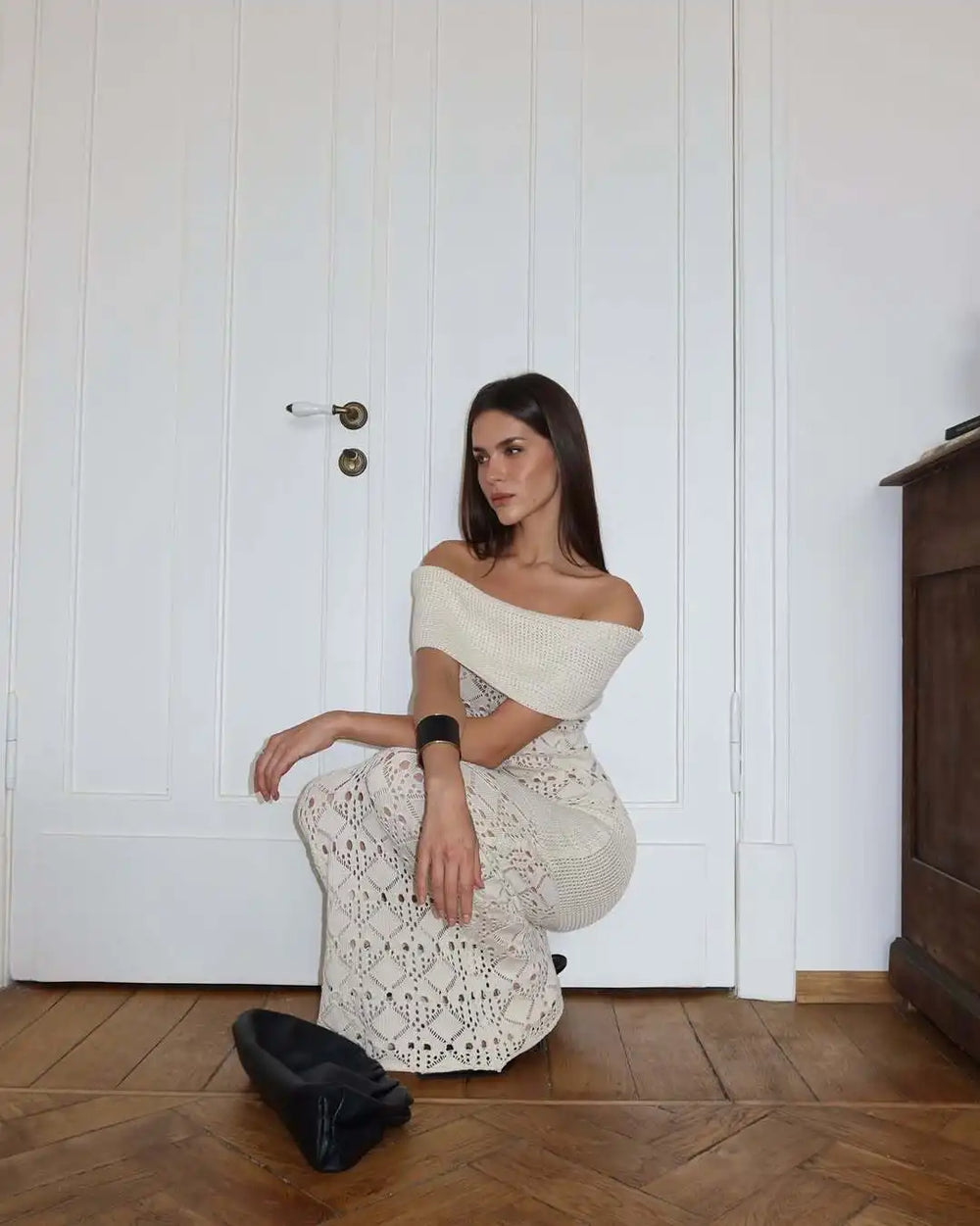 Woman in a white off-shoulder dress sitting on the floor against a white paneled wall.