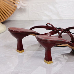 Maroon high-heeled shoes with gold toes on a light gray background