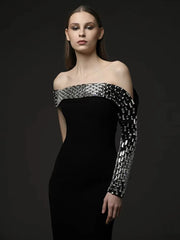 Model wearing a black off-shoulder dress with silver geometric patterns on a dark background