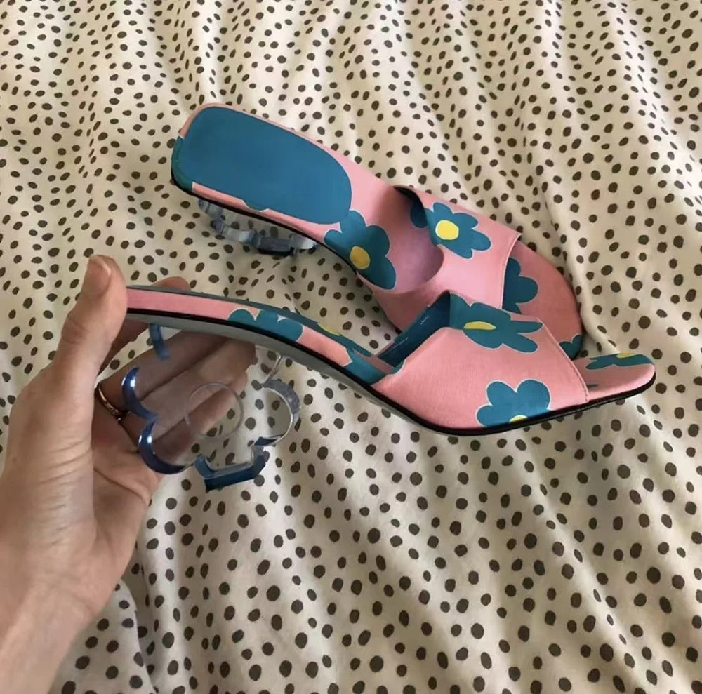 Hand holding a pink floral print mule with a clear acrylic flower heel