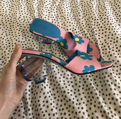 Hand holding a pink floral print mule with a clear acrylic flower heel