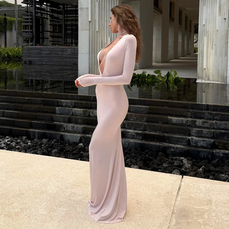 Woman in a long, light-colored dress standing outdoors near steps and water.