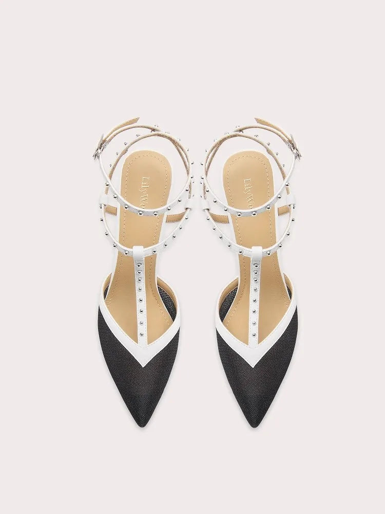 Black and white pointed-toe shoes with studded details on a light gray background