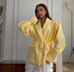 Woman wearing a yellow jacket indoors with a neutral background