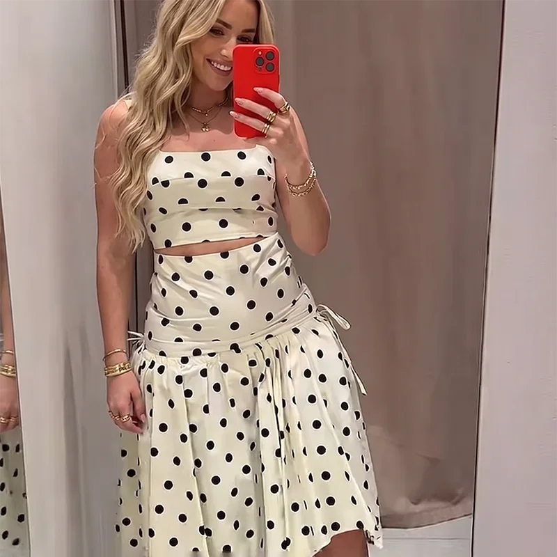 Close-up of a woman wearing a white and black polka dot print crop top and asymmetrical midi skirt.
