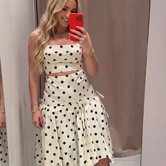 Close-up of a woman wearing a white and black polka dot print crop top and asymmetrical midi skirt.