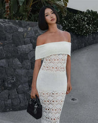 Woman wearing a white off-shoulder dress with lace details against a stone wall.