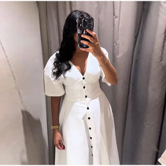 Person wearing a white dress with black buttons in front of a plain background